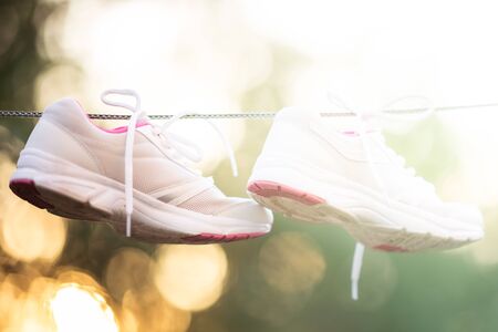 white pink female sneakers dried on a rope in the sunny summer gardenの写真素材