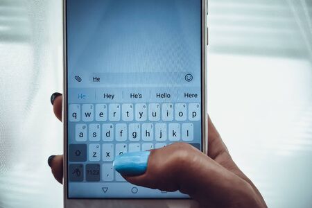 Female hand with blue nails is typing on a white smartphone a messageの写真素材