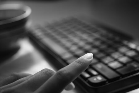 female hand is typing on the keyboard, selective focus on the finger, bw photoの写真素材