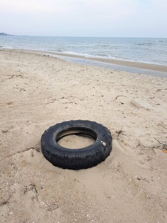 big black car tire lies on a sandy sea beachの写真素材