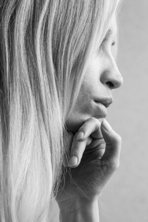 Soft portrait of a young girl with hand under her chin, side view in profile, black and white photo.の写真素材