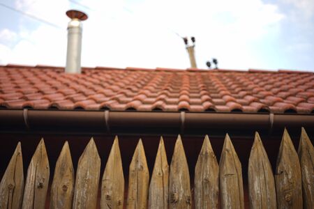 Fence made of sharp wooden stakes. Background house with red tiled roof and blue sky. Blurred.の写真素材