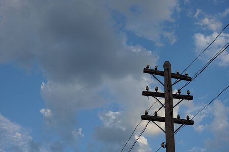 Old wooden electric pole on a blue cloudy sky background