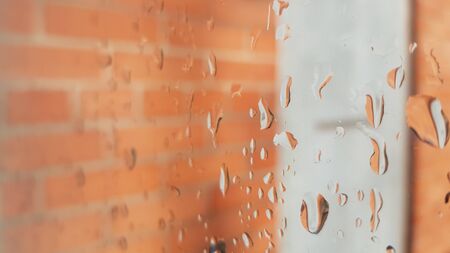Window in raindrops close-up, a drops of rain on the glass. Orange brick wall with grey door outdoor