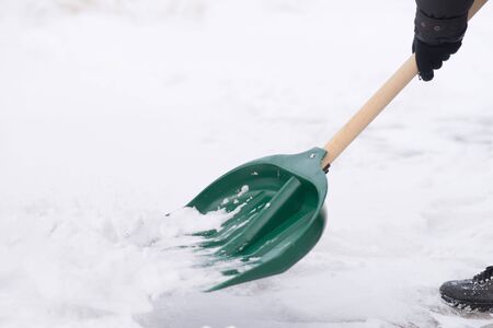 Man with snow shovel cleans pavement in winter gardenの写真素材