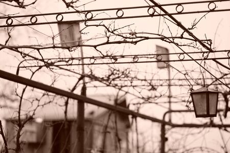 Old retro lantern hanging on a chain in the rural yard. Sepia photo