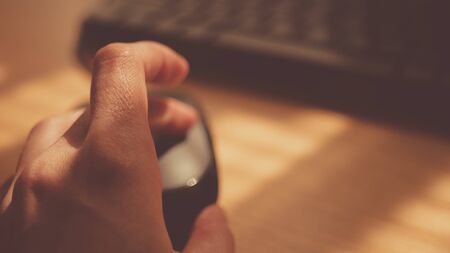 Female hand use computer mouse near keyboard, sunny desktop, selective focus on finger.