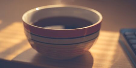 Big stripped bowl with black tea drink on sunny office table.の写真素材