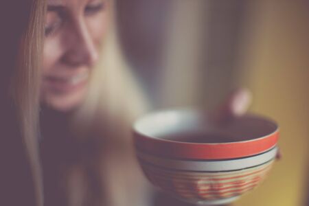 Large orange bowl with tea in hands of a smiling young woman, soft selective focus on the mug