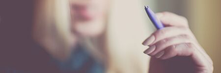 Female hand with pen in air, smiling face background, soft selective focusの写真素材