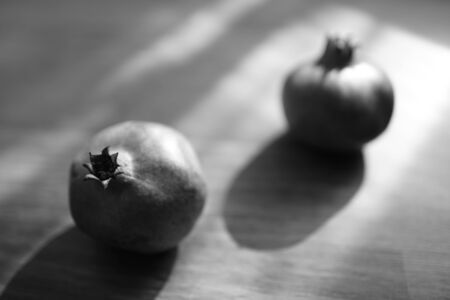 Two whole ripe pomegranate on the wooden sunny table, bw photoの写真素材