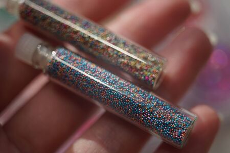 Two glass bottles with small round stones for nailart in female fingers, materials for the nail...