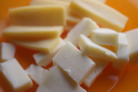 Two kinds of hard cheese on a plate close-up, rectangular slices of maasdam and cheddar