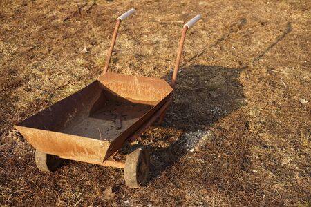 An old rusty cart on wheels stands on the ground with dry grass