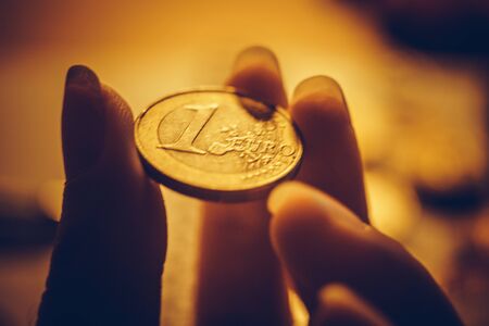 Golden 1 euro coin in female fingers closeup.