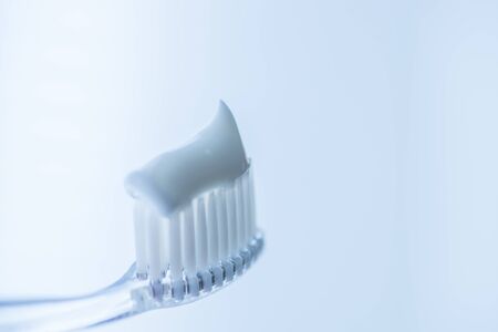 Transparent plastic toothbrush with white toothpaste on a blue white background with reflection on the glass. Macro imageの写真素材