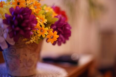 A lush bouquet of artificial flowers in a flowerpot stands on a table in the living room, close-upの写真素材