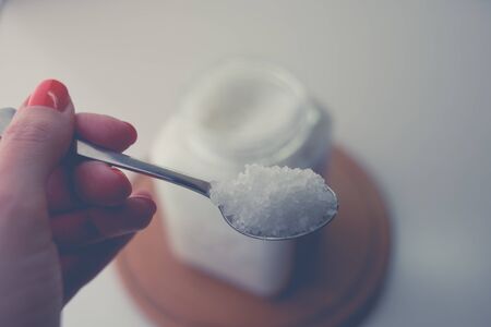 female hand holds a spoon with sea salt on the background of the container on the table