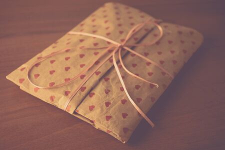 Gift in paper packaging with a pattern of red hearts on the table.