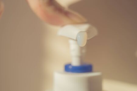 Female finger touch on a liquid soap dispenser. White gel begins to fall out of the bottle. Macro photo.の写真素材