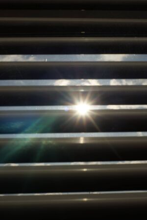 Closed blinds in dark room. Sun shine with rays outdoor.の写真素材