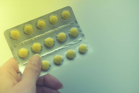Blister with yellow vitamins or pills in female fingers, copy space