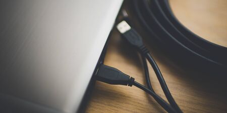 part of a silver laptop with usb wires and a skein of hdmi on a wooden table, top view.