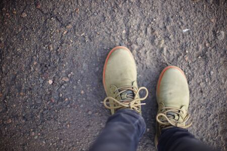 female leg in green boots and gray jeans on the asphalt road, top view.