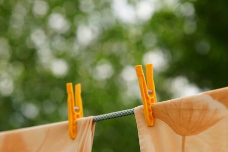 Beige clothes are dried with yellow plastic clothespins in the summer garden.の写真素材