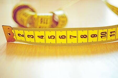 Yellow measuring tape with black scale on the wooden table. Copy space, side view
