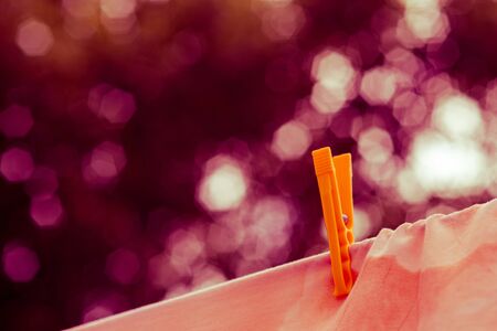 Beige clothes are dried with a yellow plastic clothespin in a summer garden, beautiful bokeh backgroundの写真素材