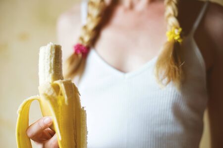 A bitten banana in a female hand. Young girl with pigtails in a white top.の写真素材