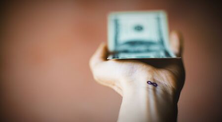 Blurred hand giving a dollar bill, on the wrist an infinity sign or number eight