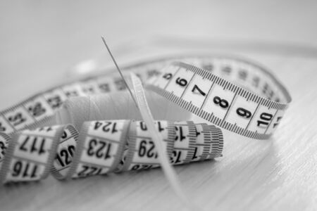 Measuring tape with black scale on the wooden table. Copy space, side view. BW photo