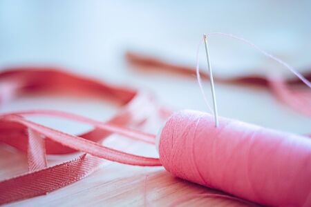 Pink spool of thread and a needle in it, side view on the tableの写真素材