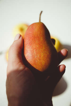 Ripe red pear in female hand. White sunny table with apples on the backgroundの写真素材