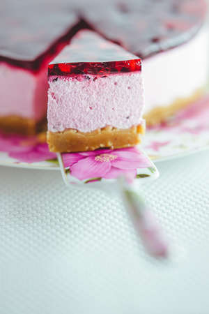 Currant cheesecake slice and whole cake in floral dish with spatula