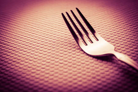 Modern silver stainless steel fork on a white table with pink lightの写真素材