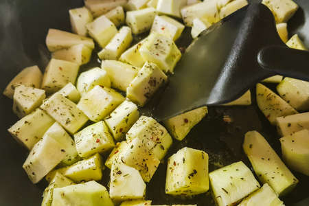 Vegetable squash in square pieces are fried in a pan. Zucchini pieces cooking with herbal spices.の写真素材