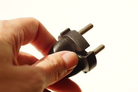 Fingers holding power plug on white background
