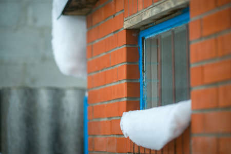 Snow caps on the windowsill. A wall with red bricks and a blue window frame with bars.の写真素材