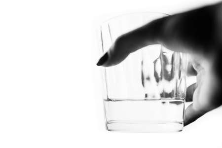A glass of water in a female hand on a white isolated background. Side view, selective focus, bw photoの写真素材