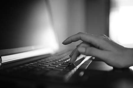 Female hand typing on a laptop keyboard. B&W photo.
