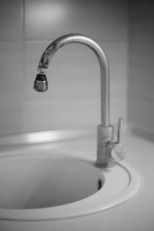 The old chrome faucet in the kitchen sink is covered in limescale. Black and white photoの写真素材