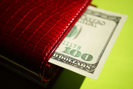 Hundred dollar bill sticking out of a red purse on a bright green table.の写真素材