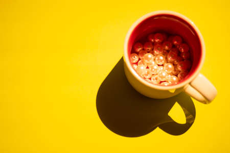 Cup with beige pearl beads inside on a yellow table. Light and shadow. Top view.の写真素材