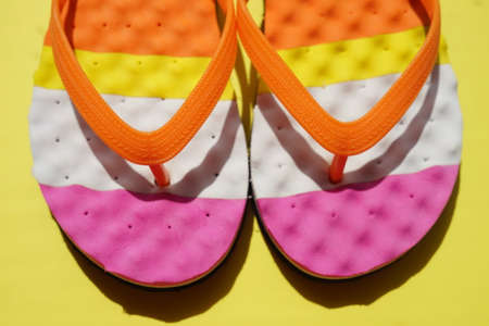 Closeup colored beach flip flops on a sunny yellow table. Top view.