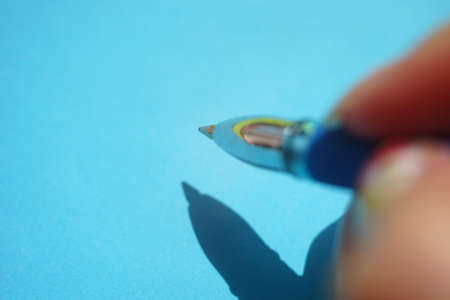 Female fingers with ball pen on a sunny blue paper with shadows.の写真素材