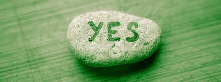 Pebble stone with the text yes on green wooden table.の写真素材