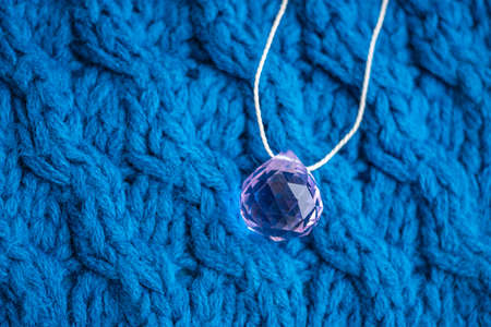 Large pink crystal with thread on a blue knitted pattern.